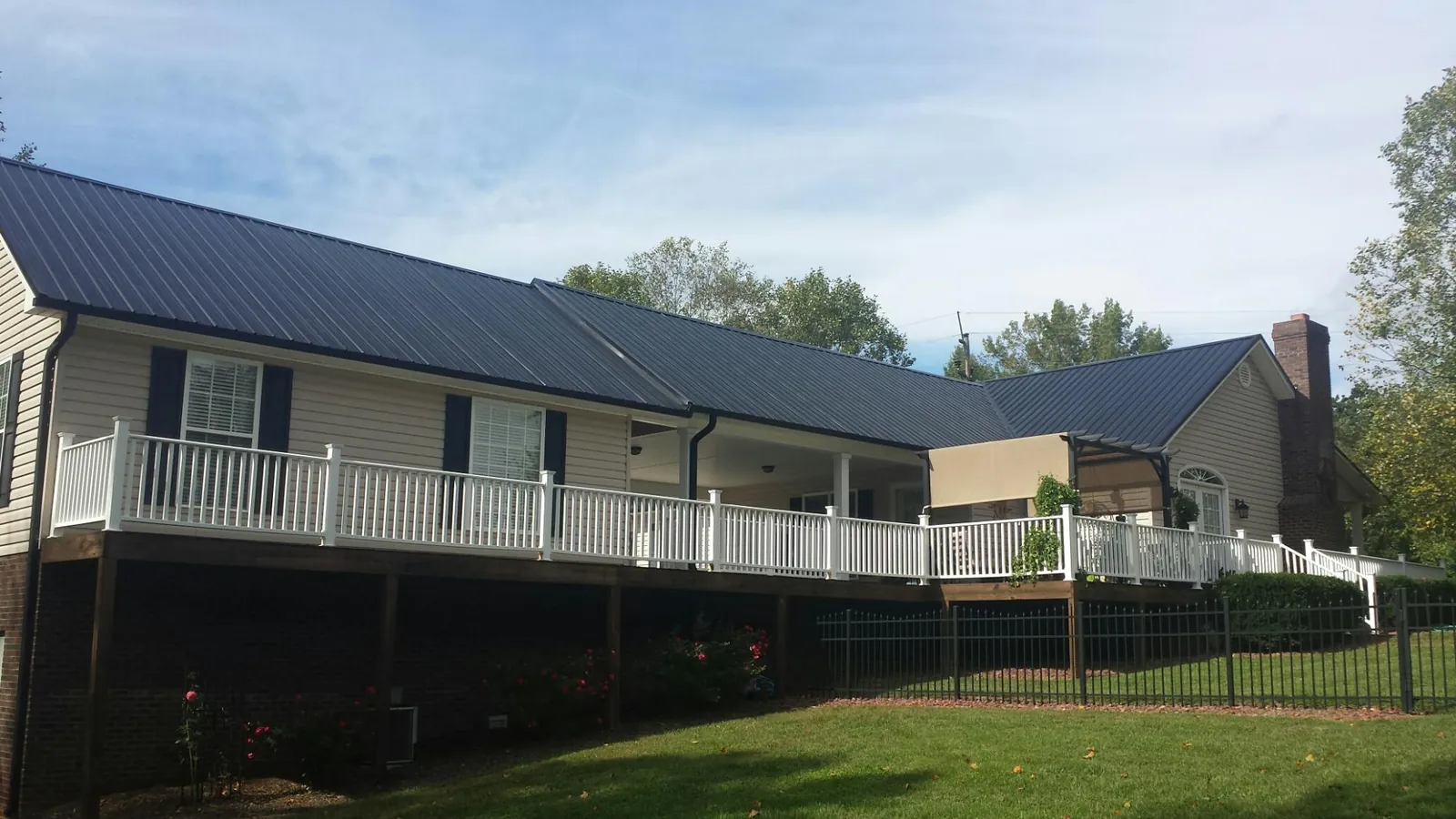 Black metal roof above a long white railed deck on a hillside home in Macon