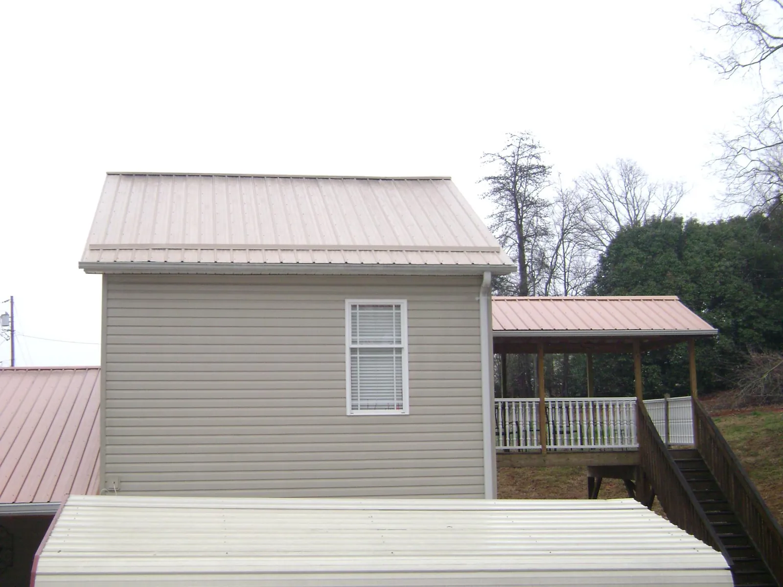 Tan metal roofs on a two story addition and attached porch, from a Roof Replacement job in Macon